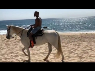 uncle floyd rides a horse along the ocean.